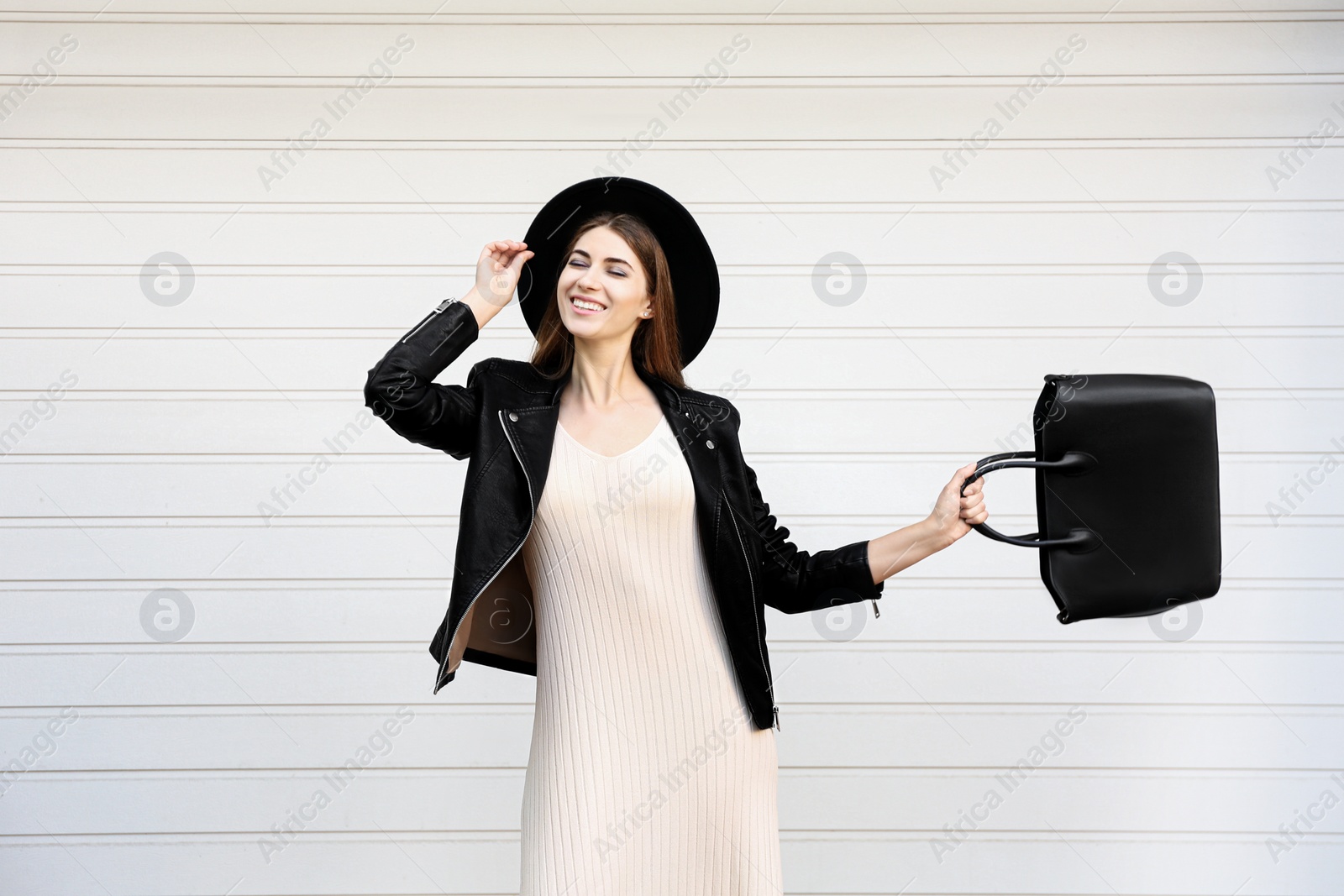 Photo of Beautiful young woman with stylish leather bag near white wall