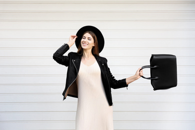 Photo of Beautiful young woman with stylish leather bag near white wall