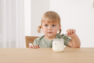 Photo of Cute little child eating tasty yogurt with spoon at wooden table indoors