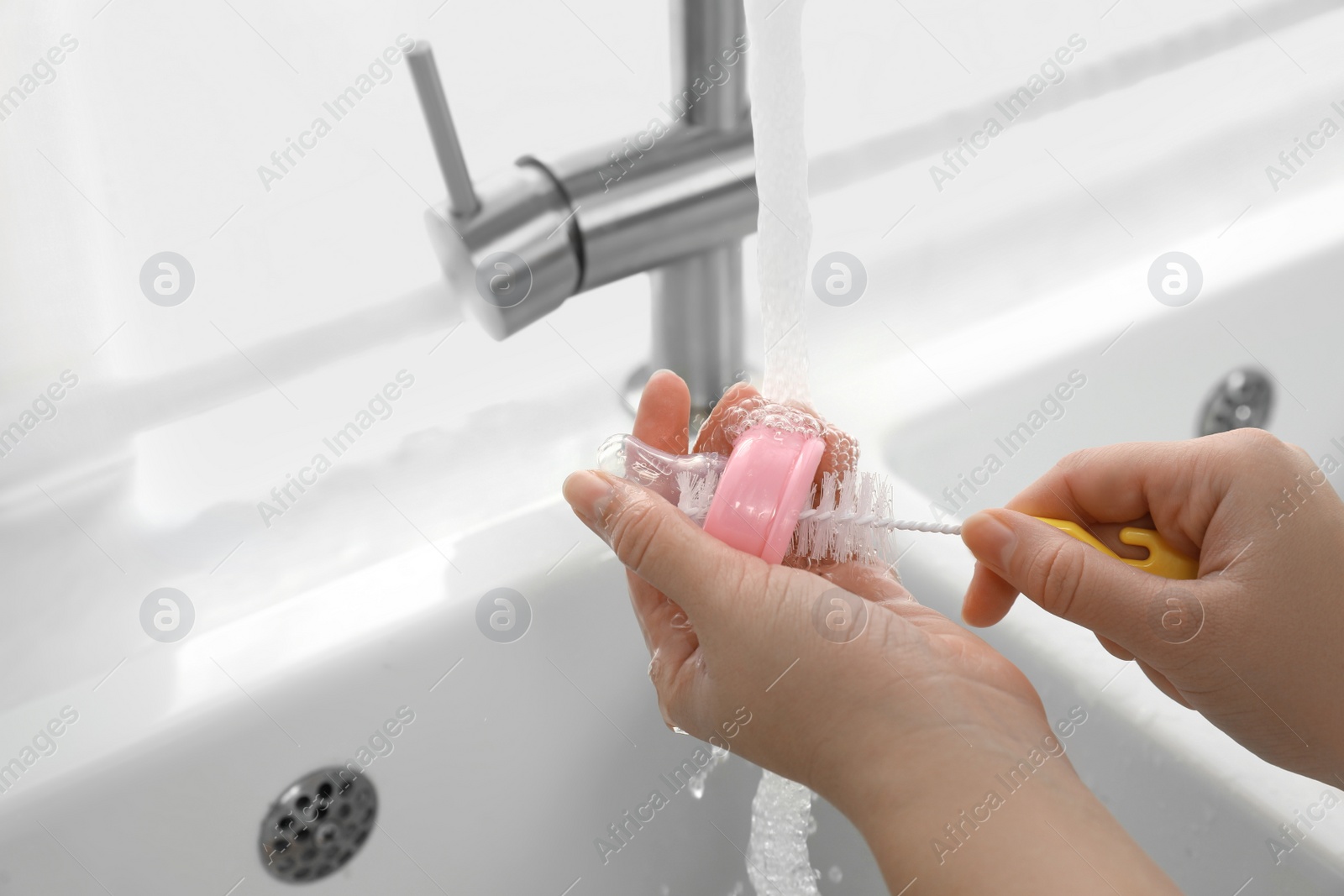 Photo of Woman washing baby bottle nipple under stream of water, closeup