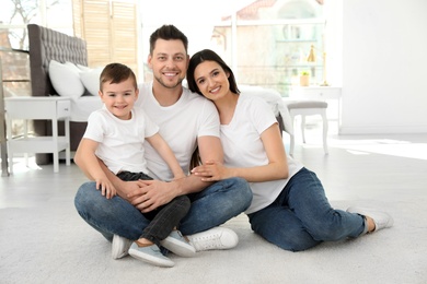 Photo of Happy parents and their son sitting together on floor at home. Family time