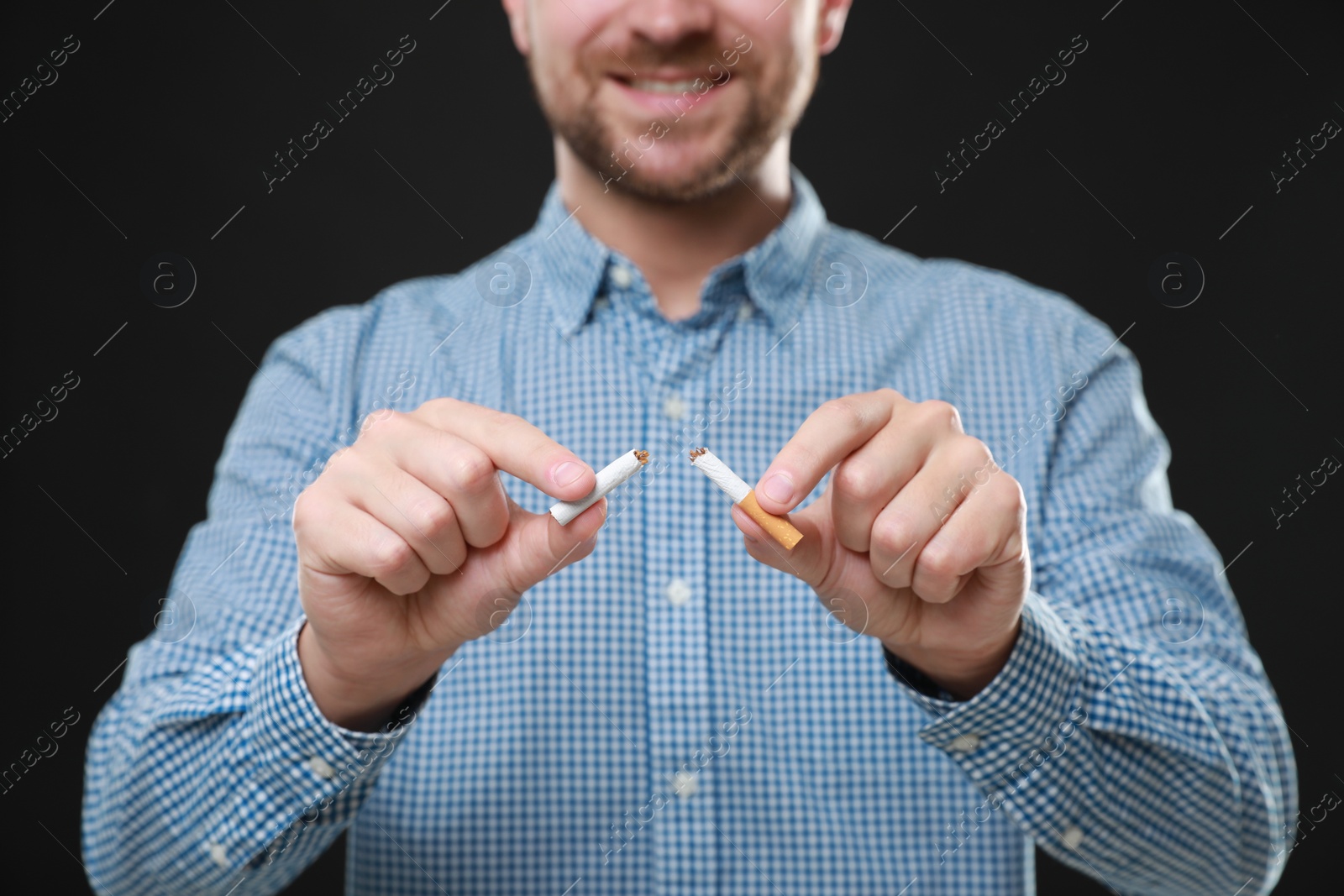 Photo of Stop smoking concept. Man holding pieces of broken cigarette on black background, closeup