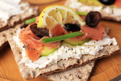 Photo of Fresh crunchy crispbreads with cream cheese, salmon, olives, lemon and green onion on wooden board, closeup