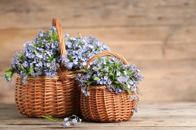 Photo of Beautiful forget-me-not flowers in wicker baskets on wooden table, closeup. Space for text