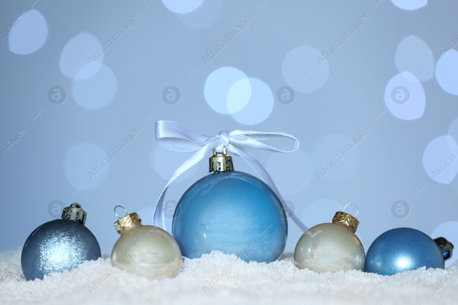 Photo of Beautiful Christmas balls on snow against blurred festive lights