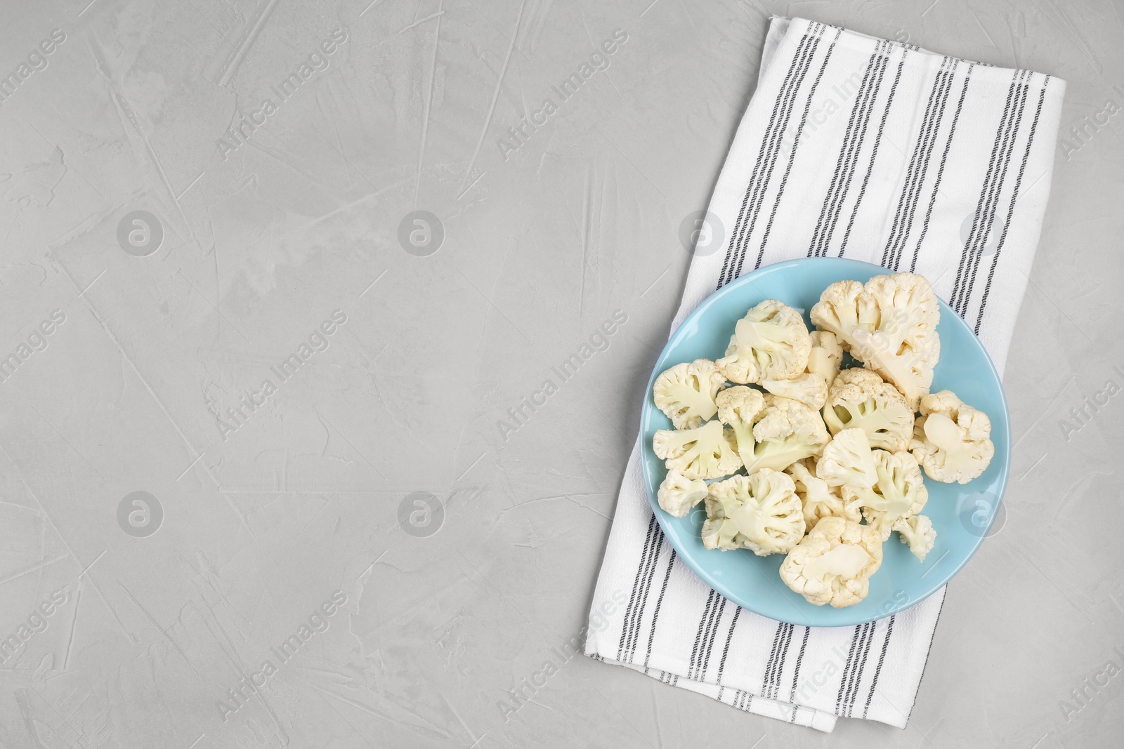 Photo of Plate with cut fresh raw cauliflower on light grey table, top view. Space for text