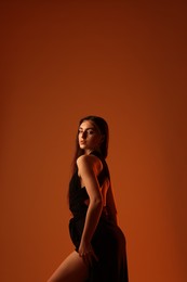 Beautiful woman in black dress posing on brown background