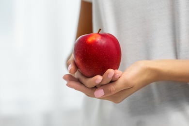 Photo of Woman holding fresh red apple on light background, closeup. Space for text