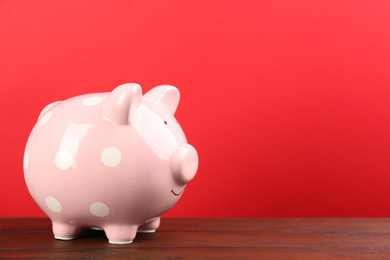 Photo of Pink piggy bank on wooden table against red background. Space for text