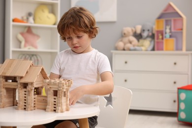 Photo of Little boy playing with wooden entry gate at white table in room, space for text. Child's toy