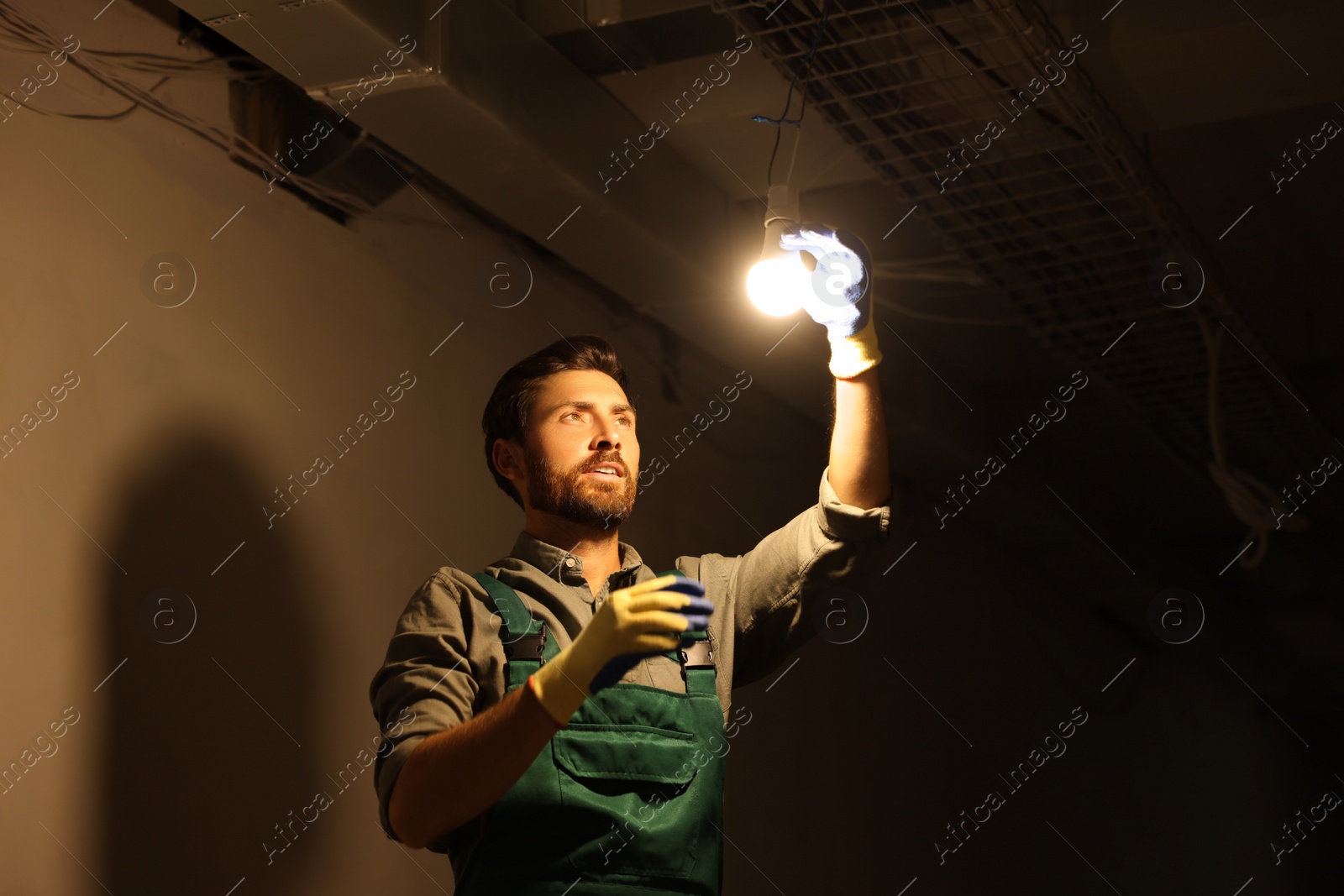 Photo of Electrician changing light bulb indoors in darkness