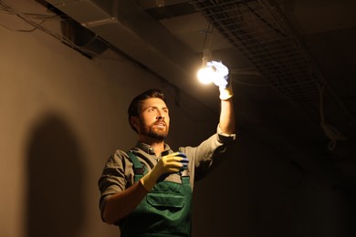 Photo of Electrician changing light bulb indoors in darkness