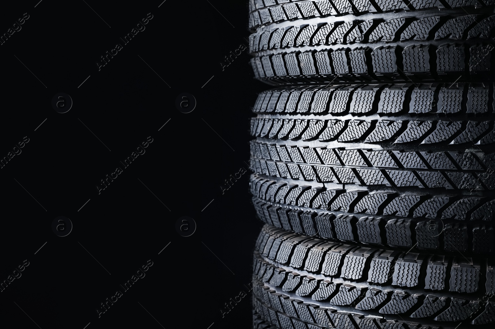 Photo of Stacked winter tires on black background, closeup. Space for text