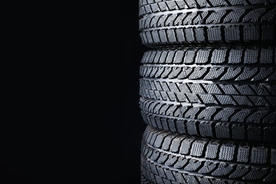 Photo of Stacked winter tires on black background, closeup. Space for text