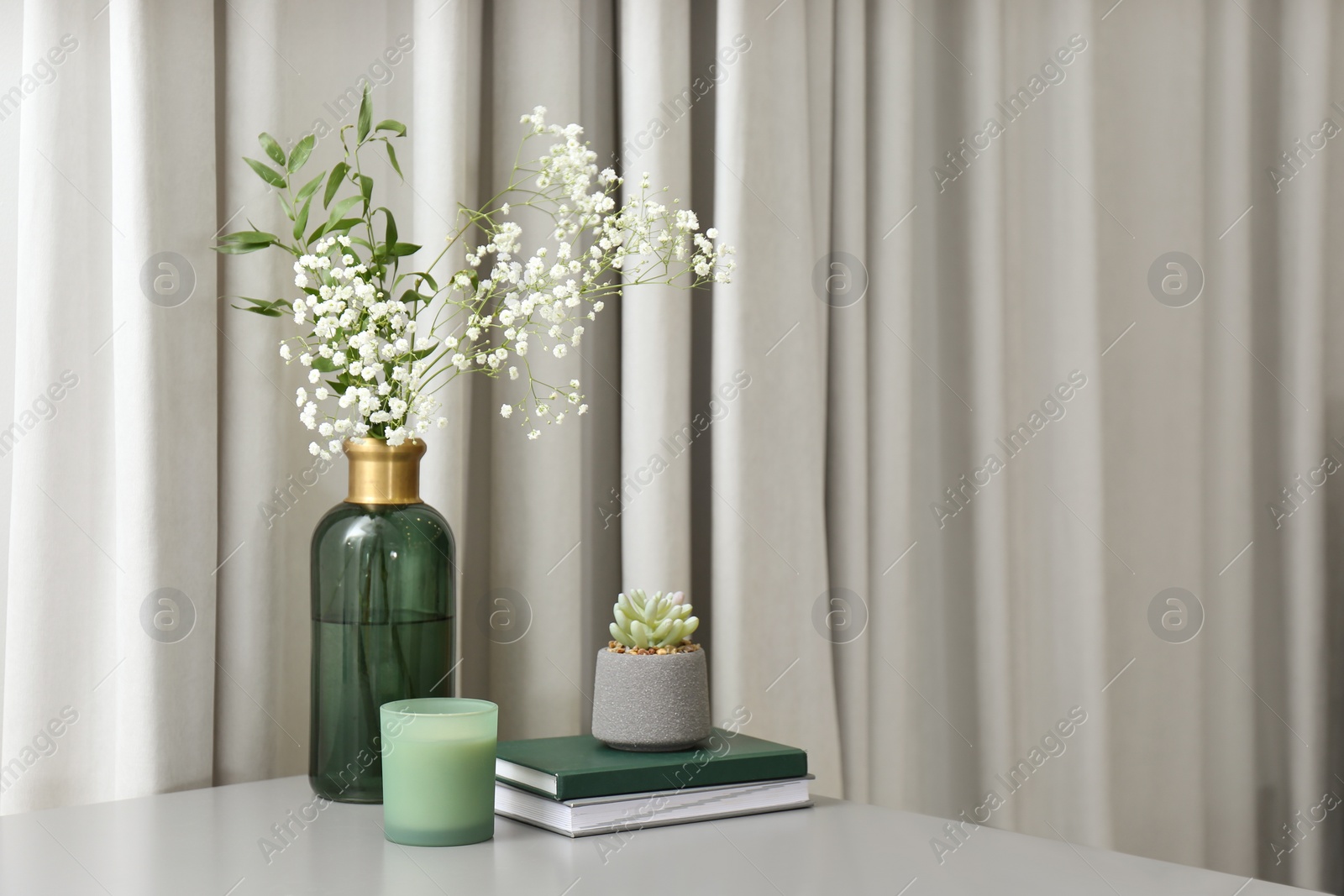 Photo of Vase with beautiful flowers, candle and books on grey table indoors, space for text. Interior elements