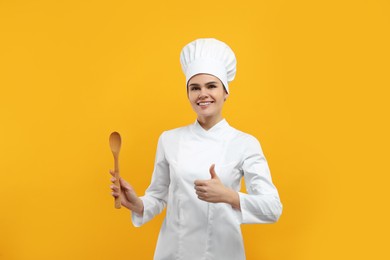 Photo of Happy chef with wooden spoon showing thumbs up on orange background