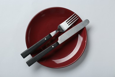 Photo of Burgundy ceramic plate with cutlery on light grey background, top view