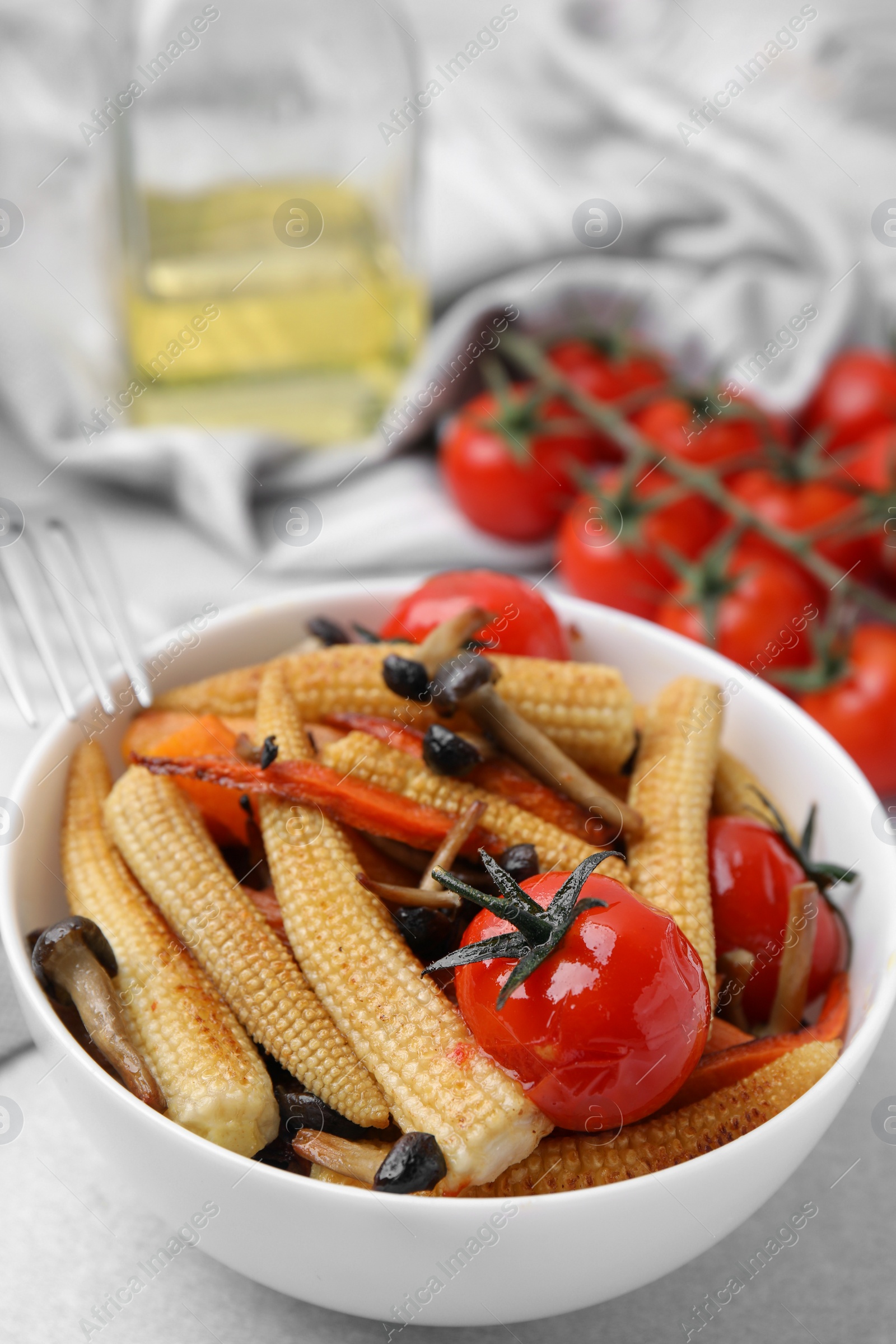 Photo of Tasty roasted baby corn with tomatoes and mushrooms on light grey table, closeup