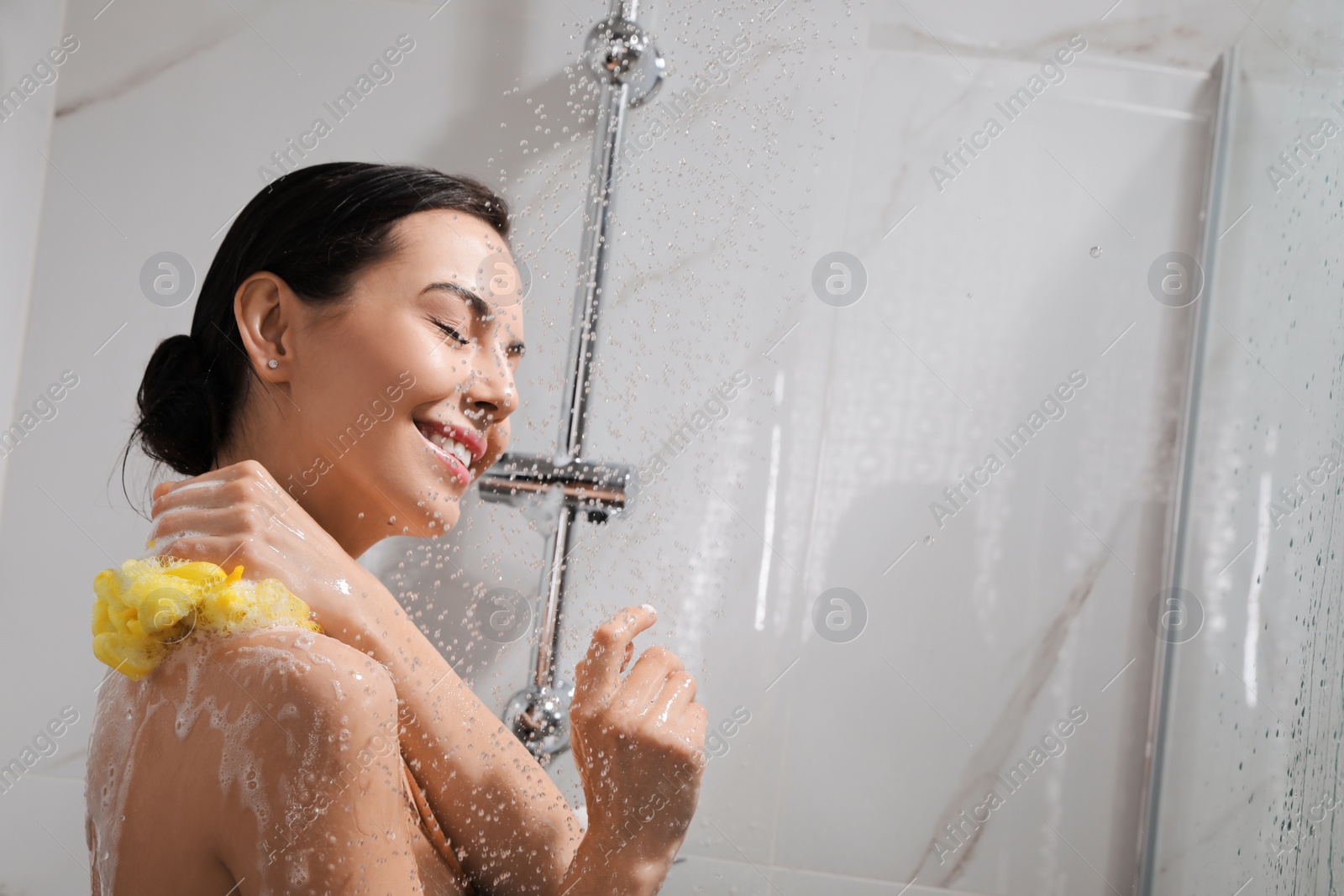 Photo of Young woman with mesh pouf taking shower at home. Space for text