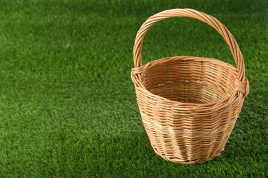 Empty wicker basket on green lawn, space for text. Easter item