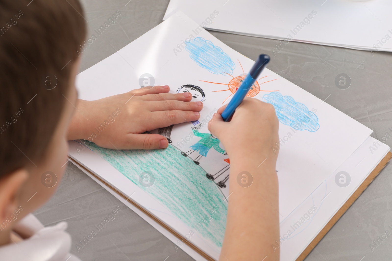 Photo of Little boy drawing with pencil at grey textured table, closeup. Child`s art