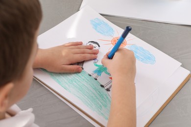 Photo of Little boy drawing with pencil at grey textured table, closeup. Child`s art