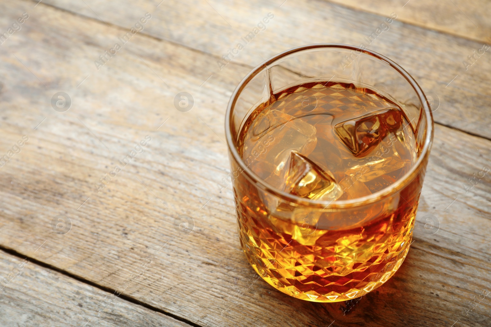 Photo of Golden whiskey in glass with ice cubes on table. Space for text