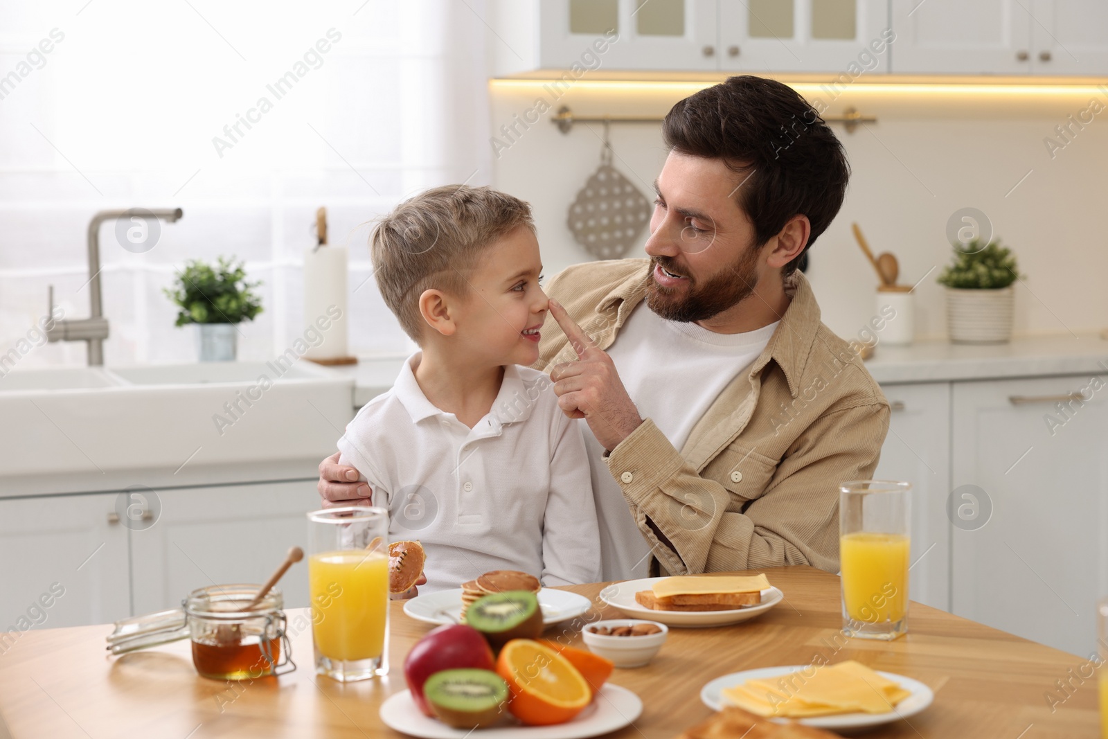 Photo of Father and his cute little son having fun during breakfast at table in kitchen