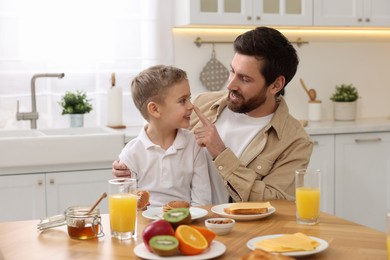 Photo of Father and his cute little son having fun during breakfast at table in kitchen