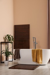 Photo of Stylish bathroom interior with ceramic tub, terry towels and houseplants