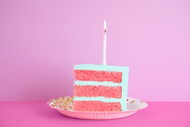 Slice of fresh delicious birthday cake with candle on table against color background