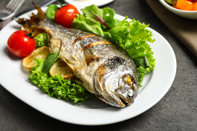 Photo of Delicious roasted fish with lemon and vegetables on dark grey background, closeup