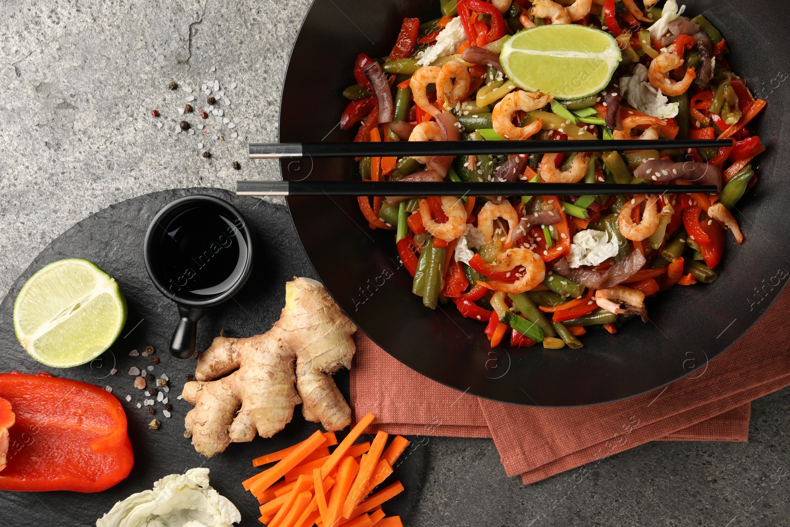 Photo of Shrimp stir fry with vegetables in wok and chopsticks on grey table, flat lay