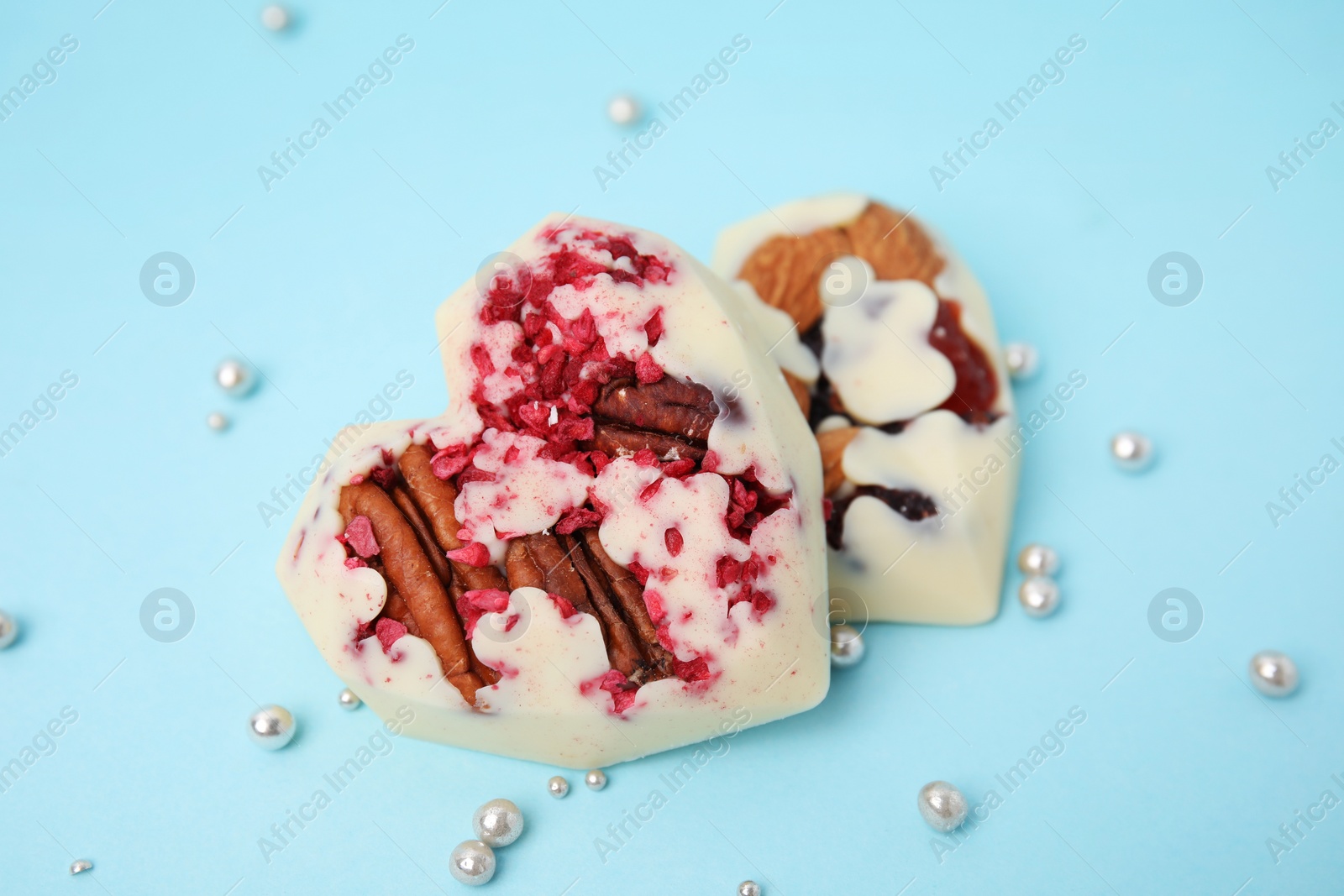 Photo of Tasty chocolate heart shaped candies with nuts on light blue background, closeup