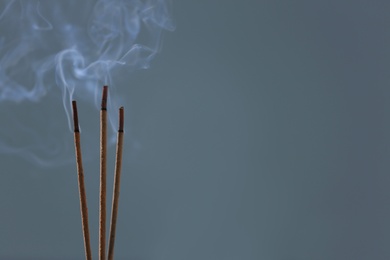 Photo of Incense sticks smoldering on blurred background, closeup. Space for text