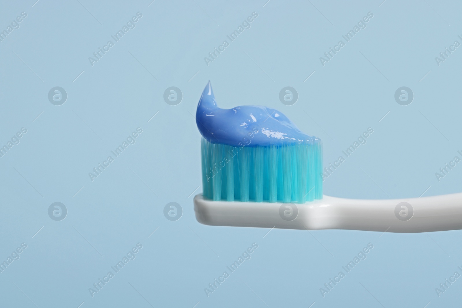 Photo of Plastic toothbrush with paste on light blue background, closeup