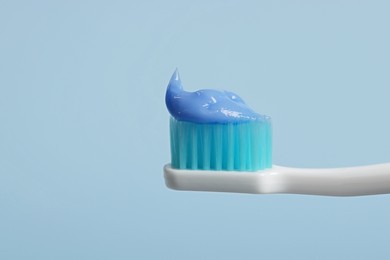 Plastic toothbrush with paste on light blue background, closeup