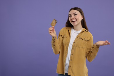 Happy woman with credit card on purple background, space for text