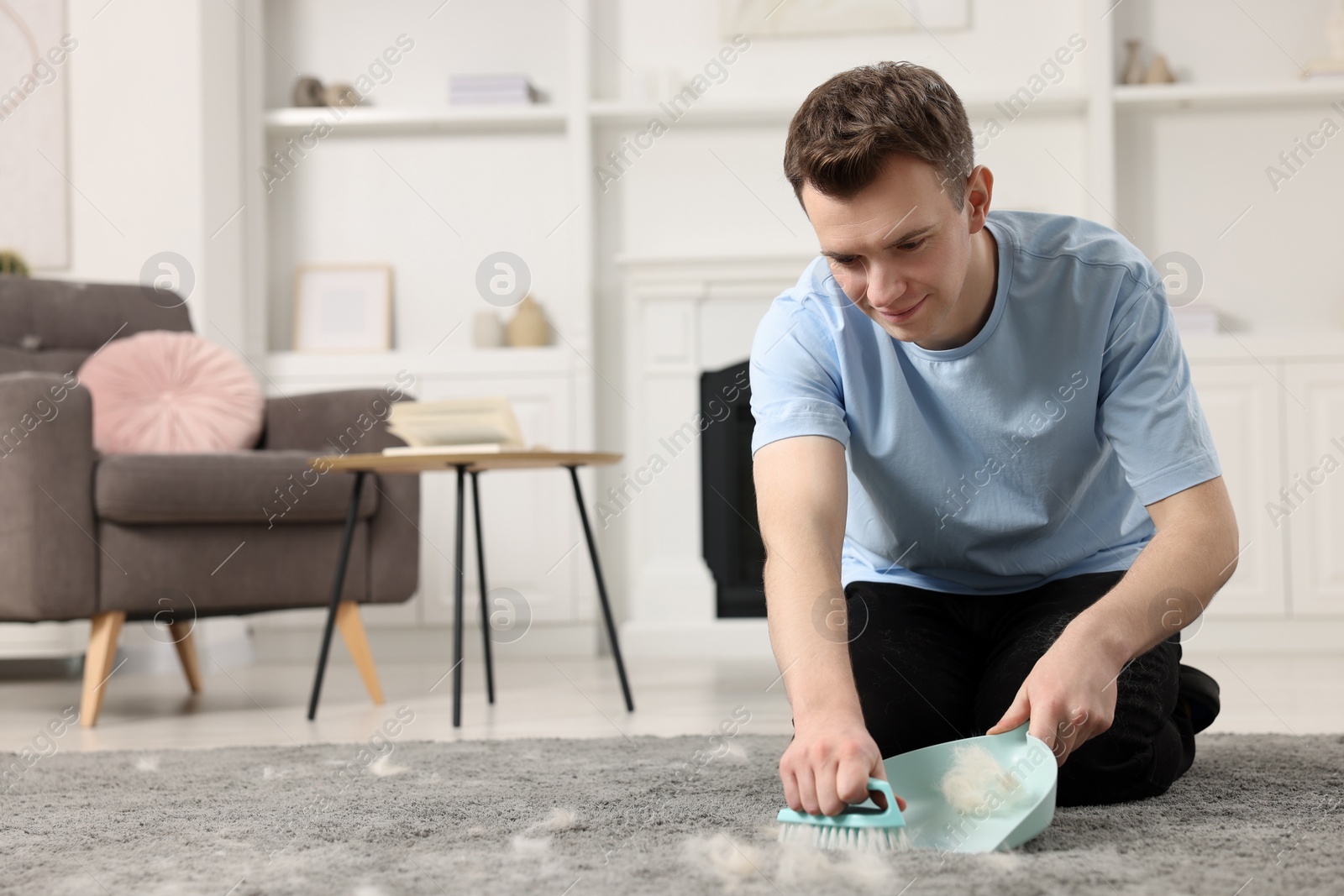 Photo of Man with brush and pan removing pet hair from carpet at home. Space for text