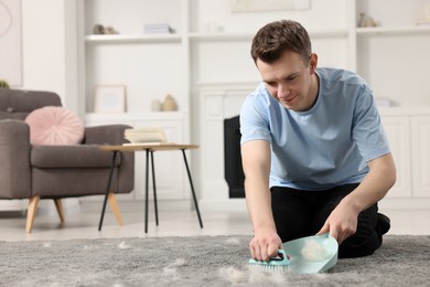 Man with brush and pan removing pet hair from carpet at home. Space for text