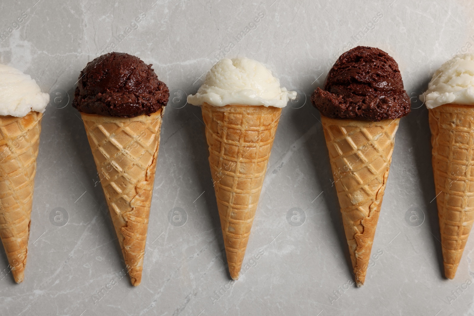 Photo of Tasty ice cream scoops in waffle cones on light marble table, flat lay