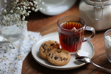 Photo of Cup of freshly brewed tea and delicious cookies on wooden table