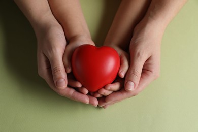 Photo of Mother and her child holding red decorative heart on light green background, top view