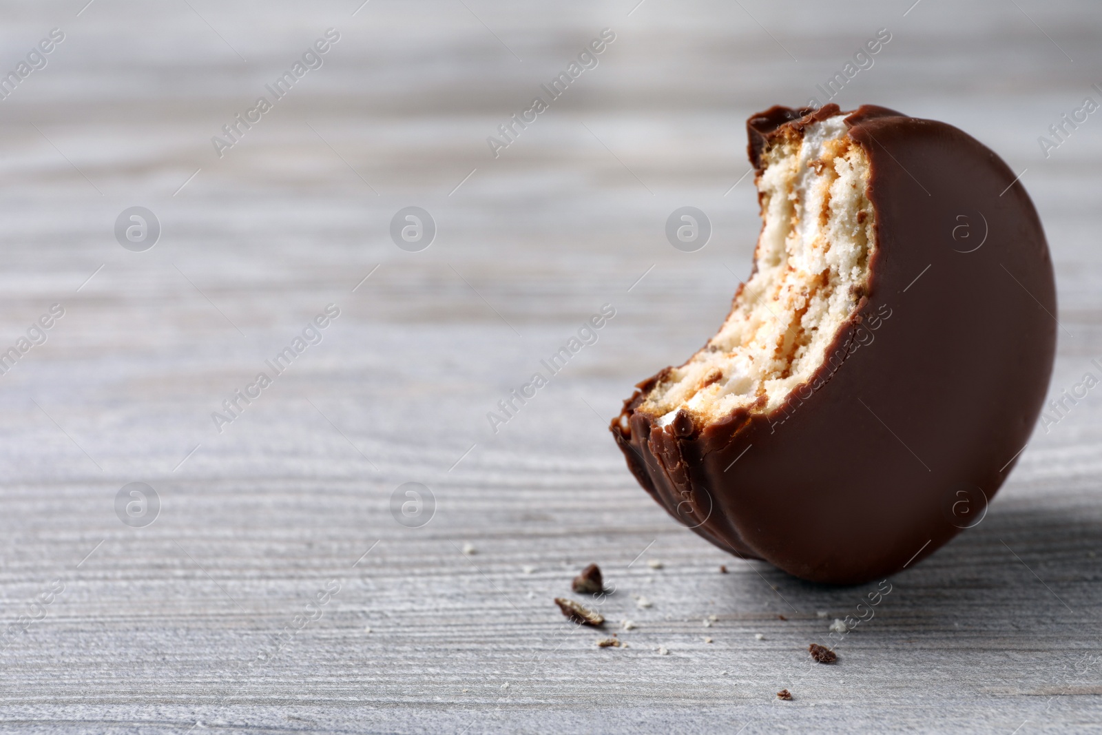 Photo of Tasty bitten choco pie on white wooden table, closeup. Space for text