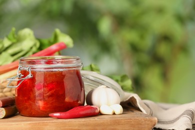 Tasty rhubarb sauce and ingredients on wooden board, space for text