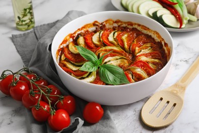 Photo of Delicious ratatouille and ingredients on white marble table