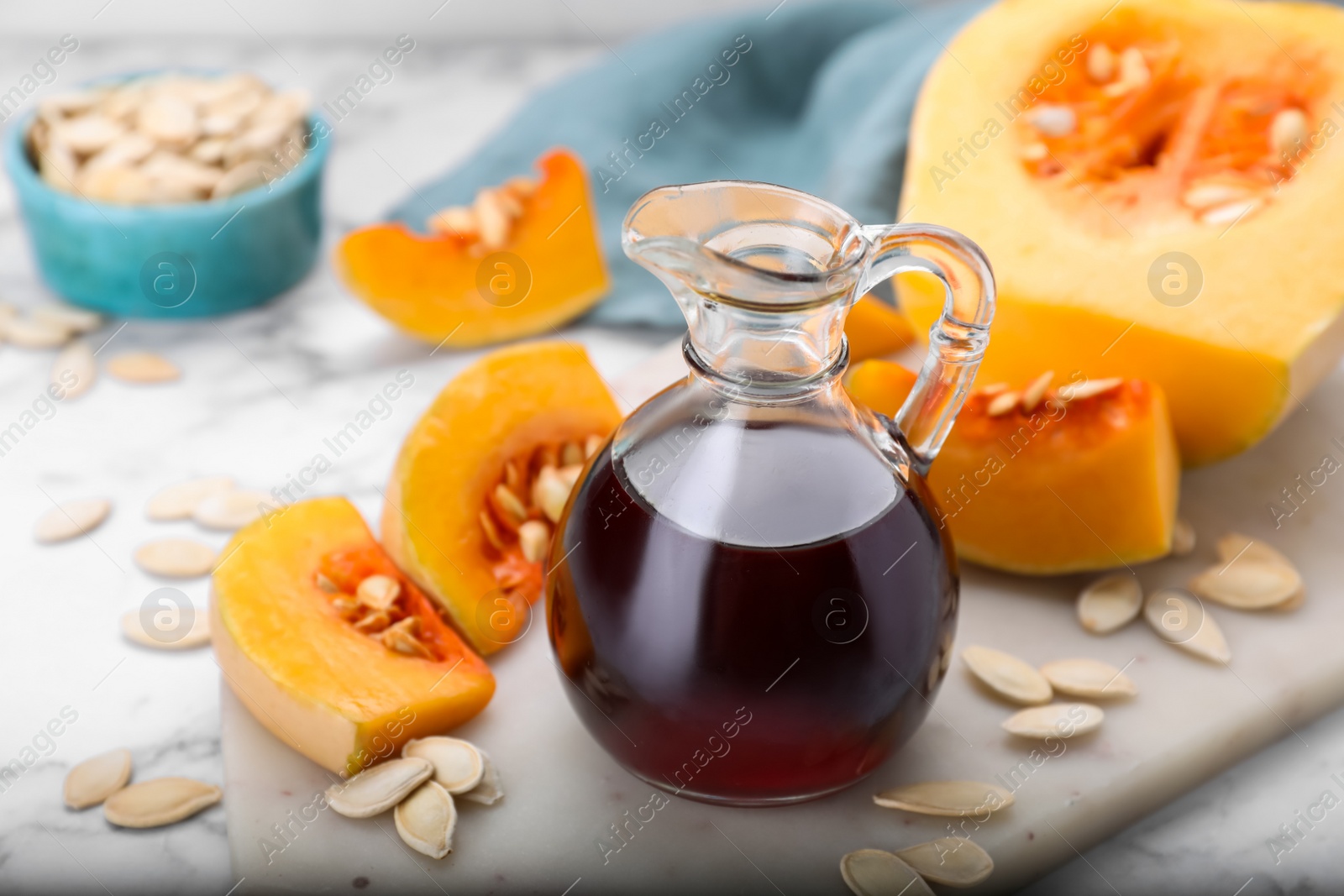 Photo of Fresh pumpkin seed oil in glass jug on white marble table