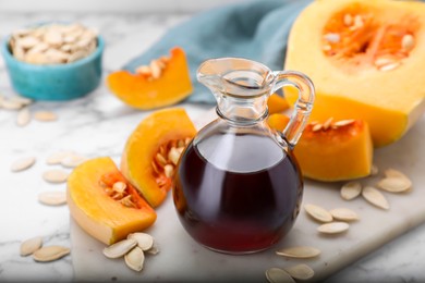 Photo of Fresh pumpkin seed oil in glass jug on white marble table