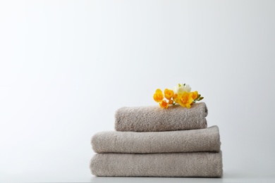 Photo of Stack of fresh towels with flowers on table against white background