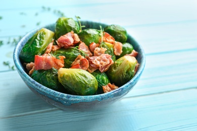 Photo of Tasty roasted Brussels sprouts with bacon on light blue wooden table, closeup